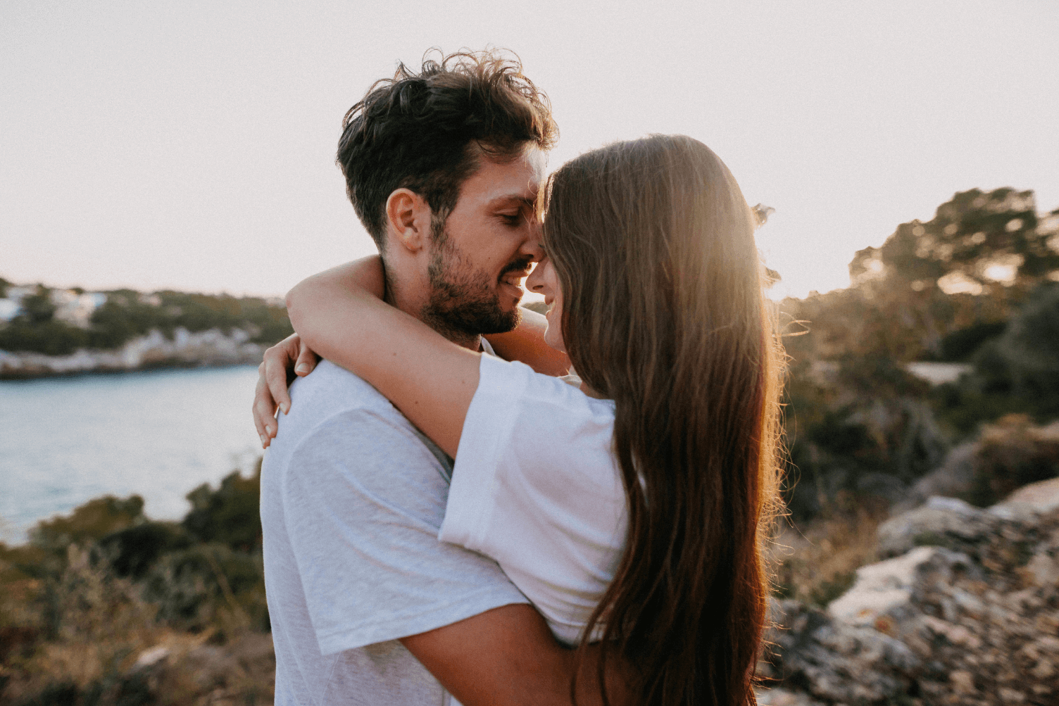 A couple embracing and sharing an intimate moment outdoors, surrounded by nature and a serene landscape.