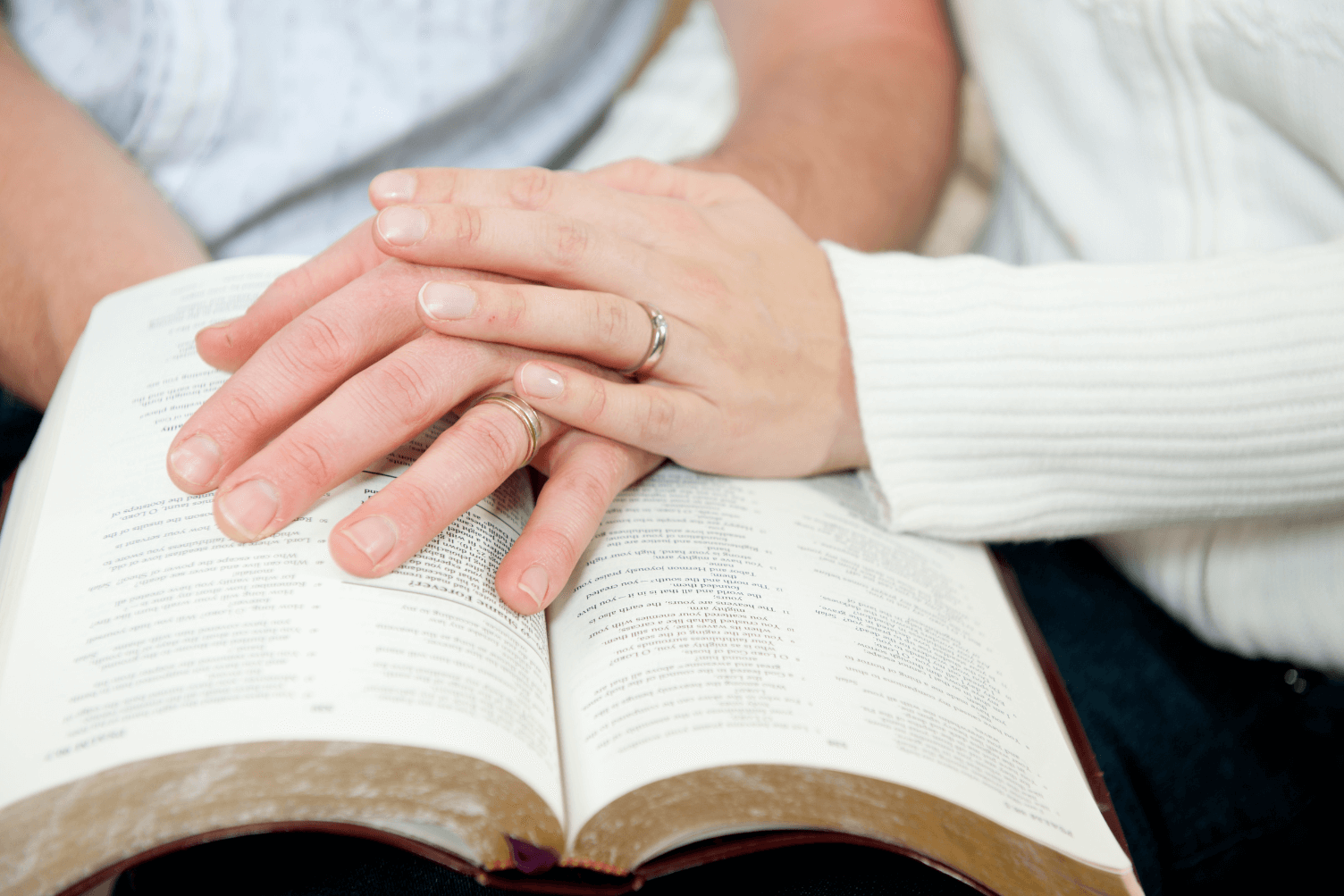 Close-up of two hands, one male and one female, resting on an open book, symbolizing connection and unity in a relationship.