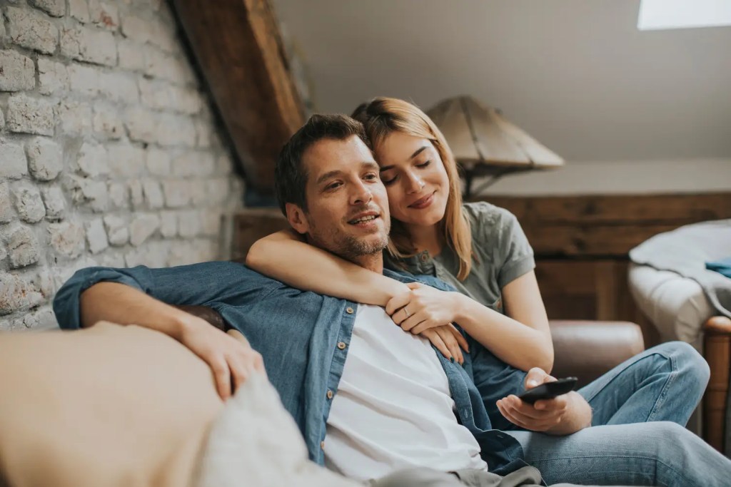 A couple sitting together on a couch, smiling and enjoying each other's company, with a cozy and intimate atmosphere in a well-lit room.