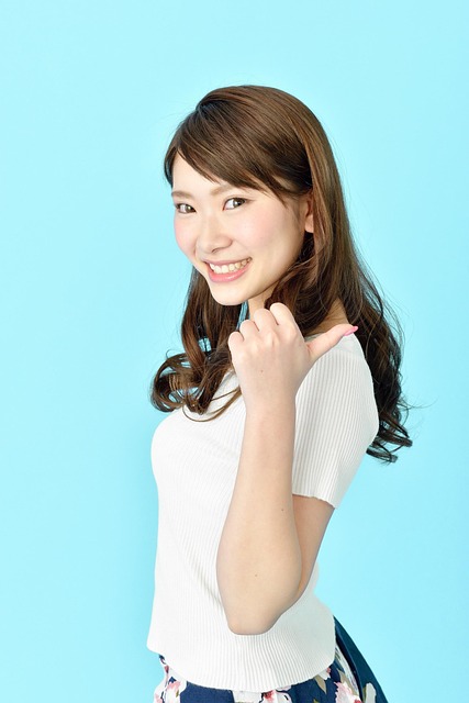 A woman with long, dark hair smiles and gives a thumbs-up gesture, standing in front of a light blue background.